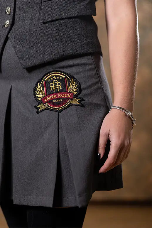 Dettaglio patch logo ricamato sulla Gonna College Anna Rock, cucitura a contrasto e pieghe ampie.