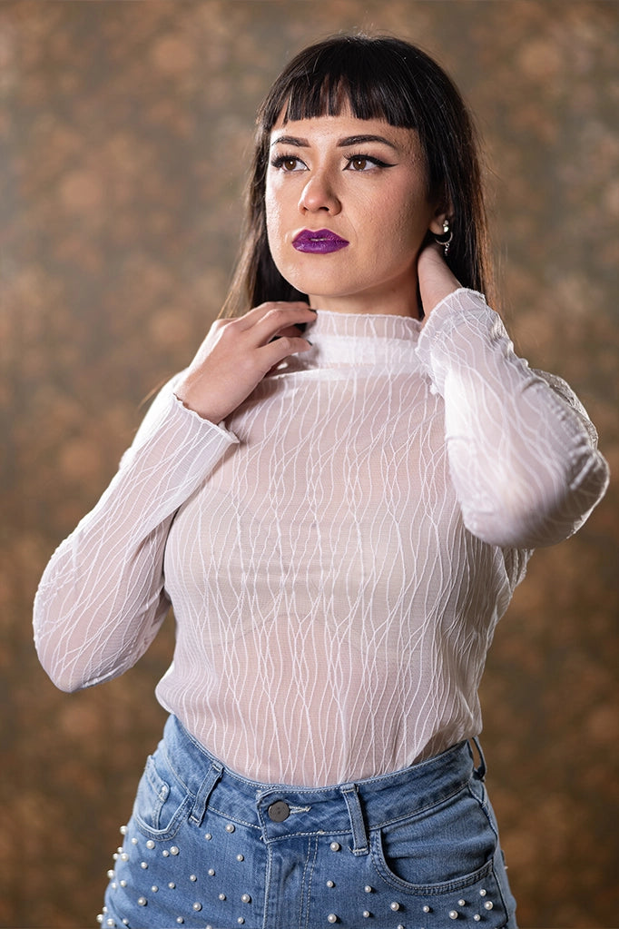Dettaglio maglia bianca in tulle con collo alto, indossata da modella con trucco marcato