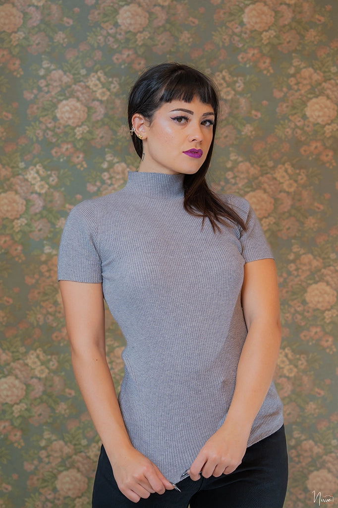 Modella indossa maglia grigia a manica corta Anna Rock, ripresa frontale con sfondo floreale vintage