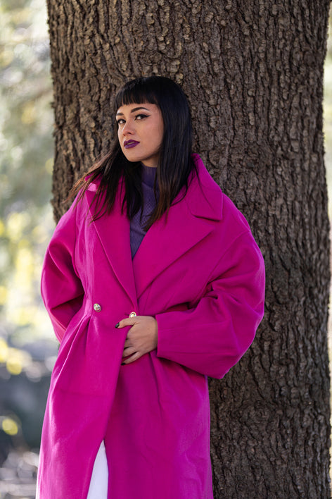 Cappotto fucsia con spalla cadente e chiusura doppio petto, modella accanto a un albero