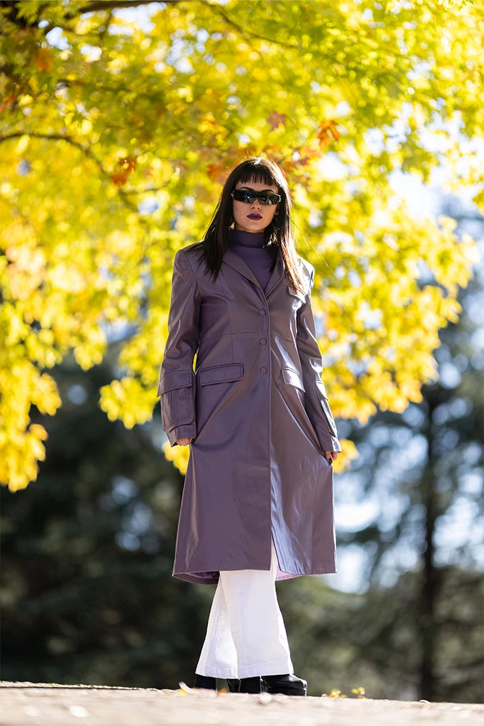 Donna indossa trench lilla in ecopelle Lumina, outfit autunnale su sfondo alberato